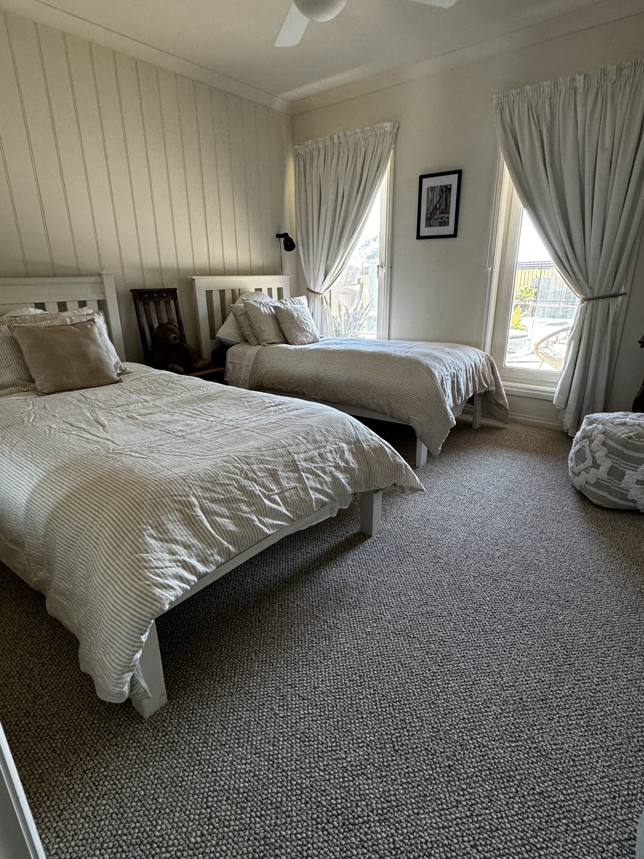 A twin bedroom with panelled walls, neutral linen and window light
