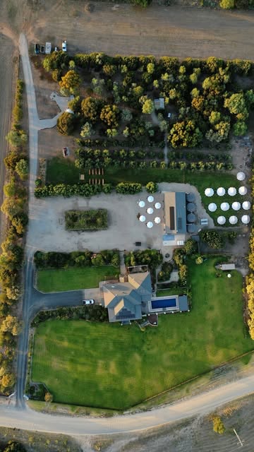 An aerial view of the whole property, showing the lodge and pool, the wedding shed and a ring of white glamping domes and bell tents set up across the paddock